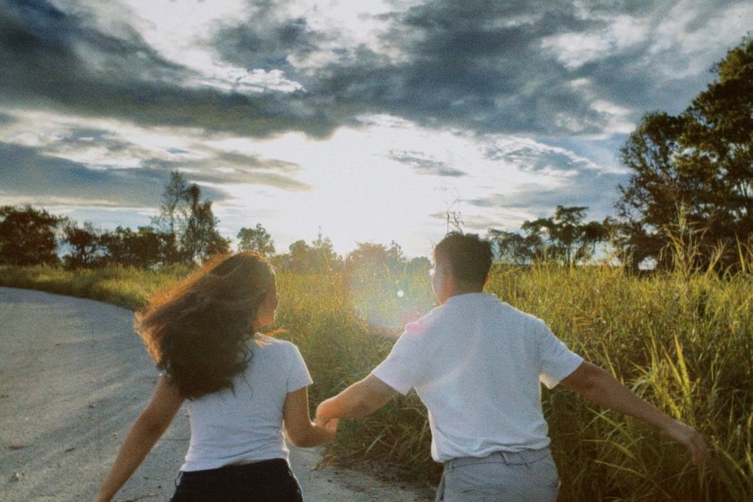 Artemus and Eleanor running hand in hand along a country road toward the setting sun